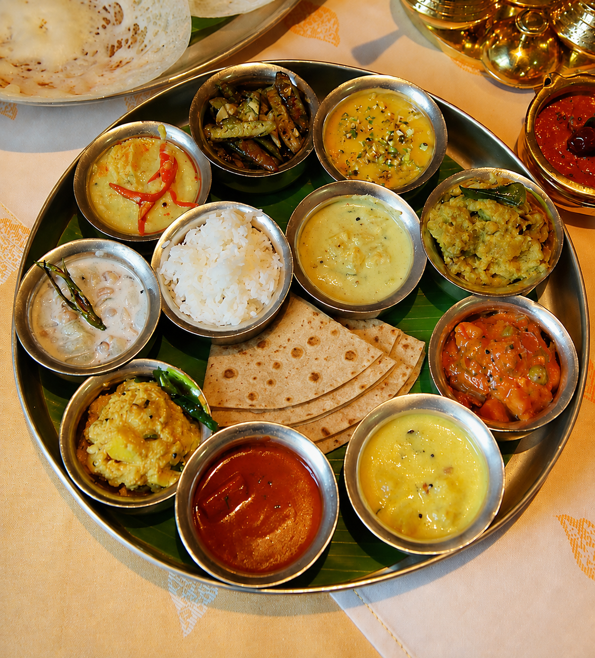 A flatlay of brass thalis with puri, dal, rice, paneer, gulab jamun and marigold petals